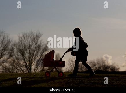 Femme Slhouette de pousser un enfant dans un landau de marcher le long d'un chemin à l'air libre avec un pays skyline Banque D'Images