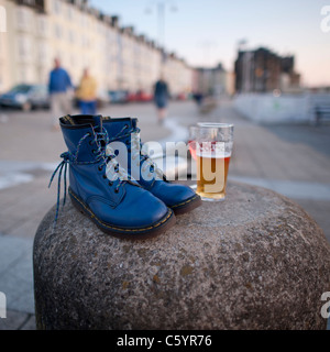 Une paire de doc marten bleu classique à lacets Bottes et une pinte de bière blonde sur la promenade de Aberystwyth, Pays de Galles, Royaume-Uni Banque D'Images