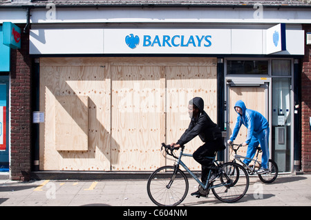 Deux jeunes sur les vélos passent la banque Barclays sur Walthamstow High Street, barricadés après l'émeutes de Londres le 8 août 2011. Banque D'Images