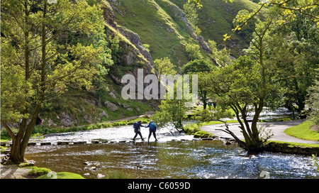 Un couple de marcheurs lutte pour traverser les pierres de gué sur la rivière Dove à Thorpe Cloud en Dovedale Derbyshire Banque D'Images