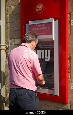 Homme mûr un retrait d'argent d'ATM machine à Moreton in Marsh dans les Cotswolds en Juillet Banque D'Images