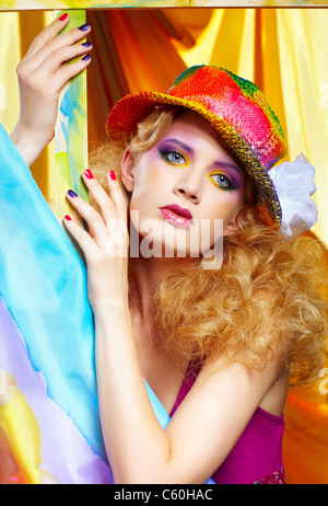 Portrait de belle blonde femme artiste en chapeau coloré debout derrière le chevalet avec tissu peint sur elle Banque D'Images