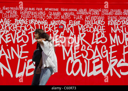 Jeune couple en passant devant le graffiti comme annonce dans Paris France Banque D'Images