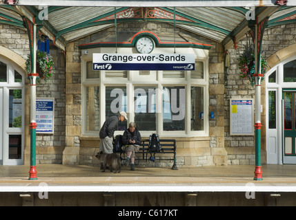 Deux personnes - et le chien - l'attente sur la plate-forme de Grange-over-Sands railway station, South Lakeland, Cumbria, Angleterre, Royaume-Uni Banque D'Images