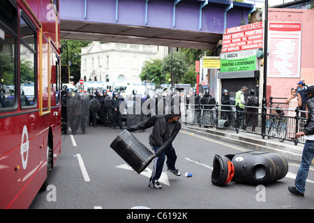 Une jeunesse à capuchon se prépare à lancer un hackney bin à la police anti-émeute sur Mare Street, Londres Banque D'Images