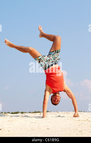 Guy Standing énergique sur les armes sur le sable avec jambes étendues Banque D'Images