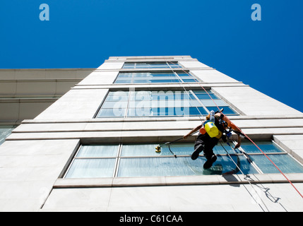 Un nettoyant de belles descentes en bas de la façade d'un immeuble à Lisbonne, Portugal lors du nettoyage de fenêtres de bureau Banque D'Images