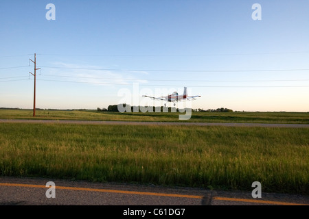 Petit Cessna A118b cropdusting les aéronefs volant bas au-dessus de l'autoroute et la poussière des champs sous les fils d'électricité Dakota du Nord usa Banque D'Images