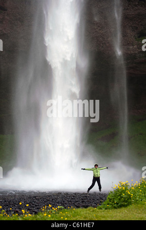 Jeune femme de sauter devant la cascade de Seljalandsfoss, Islande Banque D'Images
