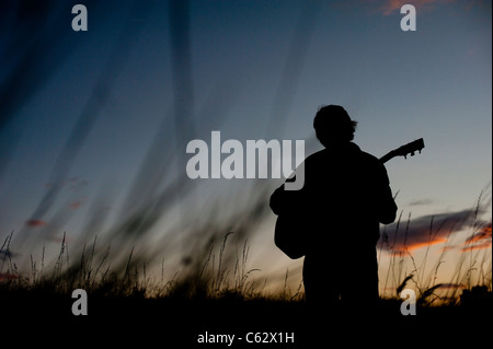 Silhouette d'un homme qui joue de la guitare dans un champ au coucher du soleil Banque D'Images