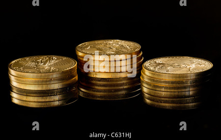 Close up of a solid gold eagle one ounce coin empilées sur d'autres jetons et reflétée dans la surface noire Banque D'Images