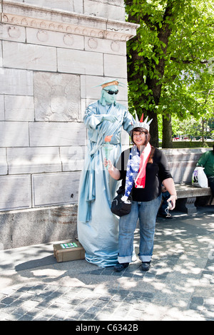 Touriste porte couronne & détient en altitude de la flamme smiling saucily comme elle pose à côté de mime déguisé en statue de la liberté New York Banque D'Images