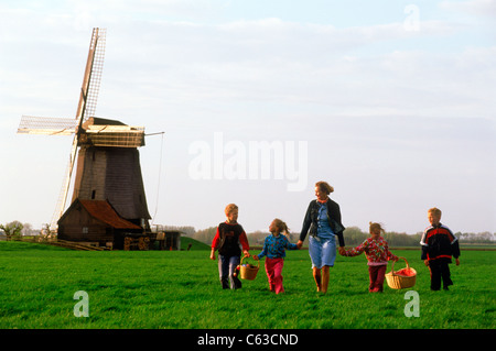 La mère et les enfants avec des paniers traversant les terres agricoles en Hollande près de Windmill Banque D'Images