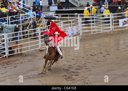 Le Stampede de Calgary, Alberta, Canada. Une jolie dame rides autour de l'infield avec un drapeau du Stampede de Calgary à l'état humide et boueux. Banque D'Images