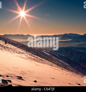 Winters soleil du soir au large de la neige a couvert Helvellyn, à travers les montagnes du Parc National de Lake District. Banque D'Images