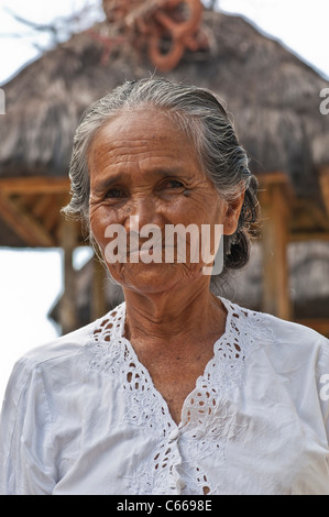 Tête et épaules prise d'une femme balinaise avec un abri traditionnel de toit de chaume hors foyer derrière. Banque D'Images
