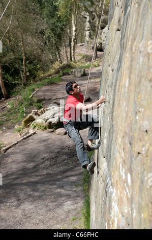 Male rock climber monte un mur presque vertical de Harrison's Rocks dans le Kent, UK, comme il est belayed par son partenaire ci-dessous. Banque D'Images