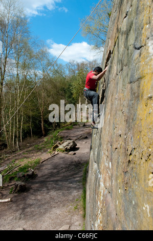 Male rock climber monte un mur presque vertical de Harrison's Rocks dans le Kent, UK, comme il est belayed par son partenaire ci-dessous. Banque D'Images