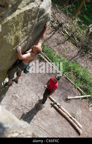 Un adulte male rock climber étant belayed à partir de ci-dessous qu'il perfectionne sa technique sur un affleurement de grès dans le Kent, au sud de Londres. Banque D'Images