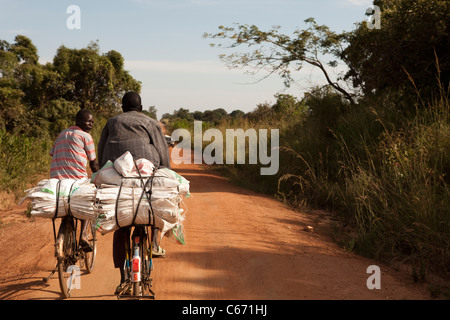 Les cyclistes traversent une route rurale à distance dans le district de Soroti, Ouganda, Afrique de l'Est Banque D'Images