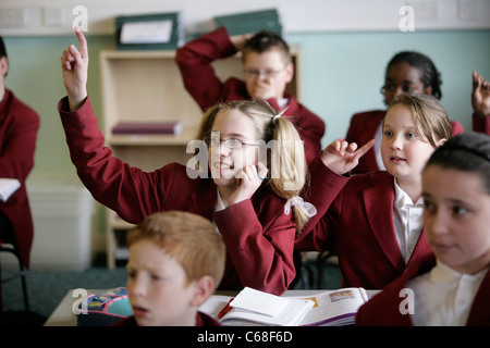 Un élève dans une école secondaire de l'UK met sa main jusqu'au cours d'une leçon pour répondre à une question. Banque D'Images