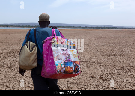 Un homme marche sur un sol sec portant deux sacs Koulikoro, Mali Banque D'Images