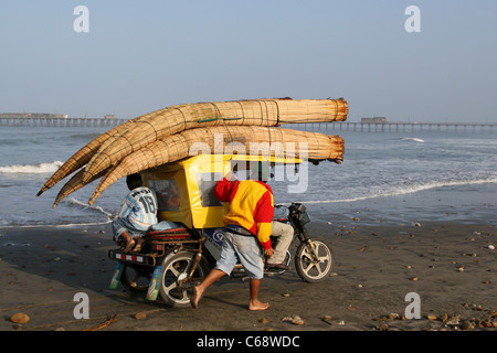 Caballitos de Totora reed bateaux chargés à bord d'un tuk tuk taxi à moteur pour le transport le long de la plage de Pimentel, le Pérou. Banque D'Images