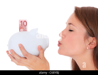 Attractive young woman kissing piggy bank. Le tout sur fond blanc. Banque D'Images