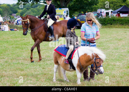 Un très jeune à l'Denmead Horse Show, est assise sur son petit poney de parler à maman. Un autre pilote sur son cheval derrière, promenades par Banque D'Images