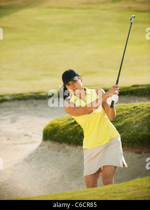 Mixed Race woman hitting balle de golf hors de bunker Banque D'Images