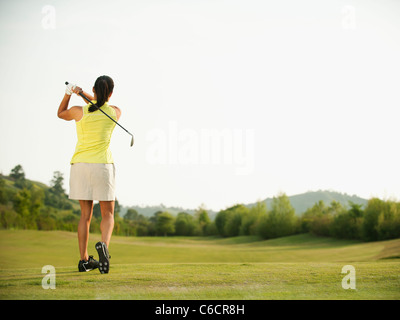 Mixed Race woman swinging golf club on golf course Banque D'Images