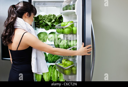 Mixed Race woman looking at légumes verts dans réfrigérateur Banque D'Images