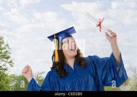 Hispanic teenage girl in graduation cap and gown holding diploma Banque D'Images