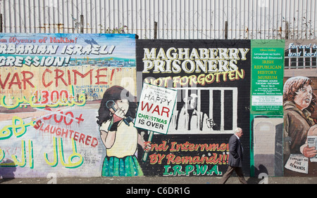 Homme marchant sur les affiches politiques passées Falls Road, Belfast, en Irlande du Nord Banque D'Images