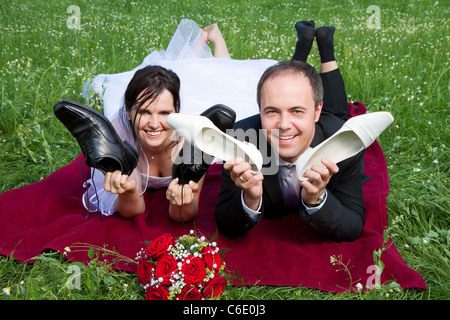 Couple de jeunes mariés avec robe de mariage costume foncé et rouge bouquet de mariée le marié et la mariée se situent sur une prairie s'amusant Banque D'Images