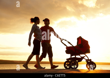 Silhouettes d'heureux parents avec poussette marche sur le littoral Banque D'Images