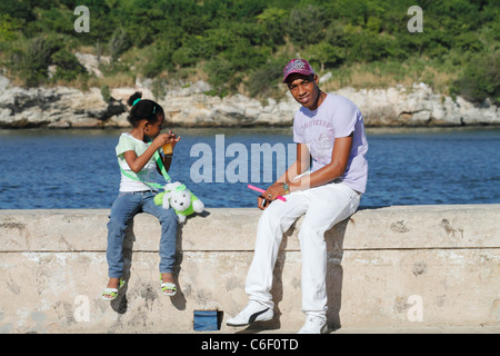 Cubain d'Afrique père et petite fille assise sur le mur et passer du temps à la rive. Malecon, La Havane, Cuba, octobre 2010 Banque D'Images