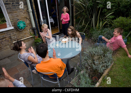 Entouré d'aussi peu d'amis, un adolescent de 15 ans souffle ses bougies portées par sa mère, dans un Londres jardin arrière. Banque D'Images