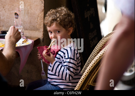 Un enfant mange et jouit d'une cuisse de poulet (jambe ou os) Banque D'Images