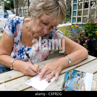 Une dame d'âge mûr écrit cartes postales de vacances Banque D'Images