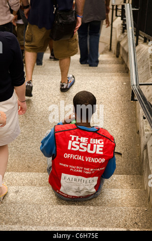 Les gens en passant devant un gros problème vendeur assis sur les marches à London UK Banque D'Images