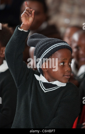 Les enfants de l'école primaire dans la classe à une école rurale avec leurs mains levées. Banque D'Images