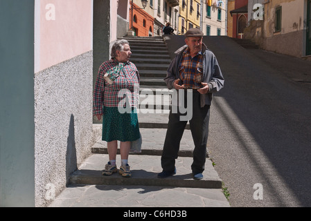 Un vieux couple italien talk et geste comme ils marchent sur le trottoir dans leur village de Riomaggiore, Cinque Terre, Italie. Banque D'Images
