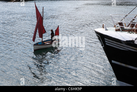 Un petit bateau à voile avec un voile rouge quitte le port de Newlyn, Cornwall Banque D'Images