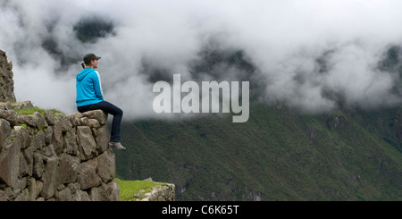 Femme assise sur un mur de pierre et à la recherche lors d'une vallée à la ville perdue des Incas, Machu Picchu, Cusco, Pérou Région Banque D'Images
