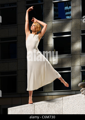 Danseuse en plein soleil posés sur des pierres ledge of office building plaza vu spectaculaire contre l'édifice sombre Banque D'Images