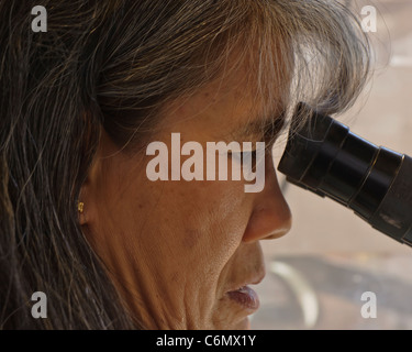 Un pairs bénévoles à travers un microscope comme elle travaille patiemment à l'aide d'un stylet pour enlever la saleté, les débris, et rock à partir d'un des combustibles Banque D'Images