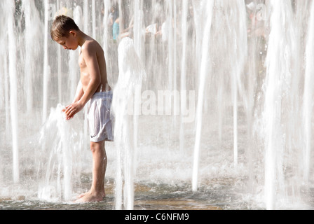 Young Boy Standing dans la Fontaine Goodwin jouer à maintenant des jets d'eau, des jardins de la paix, Sheffield UK Banque D'Images