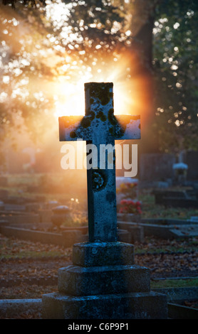 Pierres à tête de Cemetery Cross allumées tôt le matin par la lumière du soleil à travers la brume. Kings Sutton, Northamptonshire, Angleterre Banque D'Images