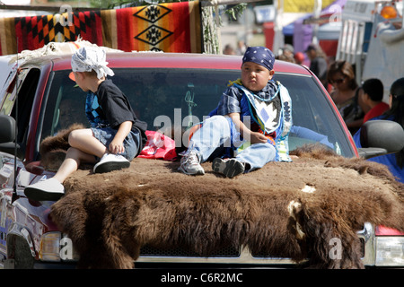 Les jeunes garçons Amérindiens à cheval sur une voiture équipée d'un bison se cacher durant un défilé tenu lors de l'Assemblée Crow juste au Montana. Banque D'Images